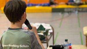 Schüler moderiert die Tischtennis-Übernachtung; auf dem T-Shirt (Rücken) ist der Schulname SRH Stephen-Hawking-Schule aufgedruckt.