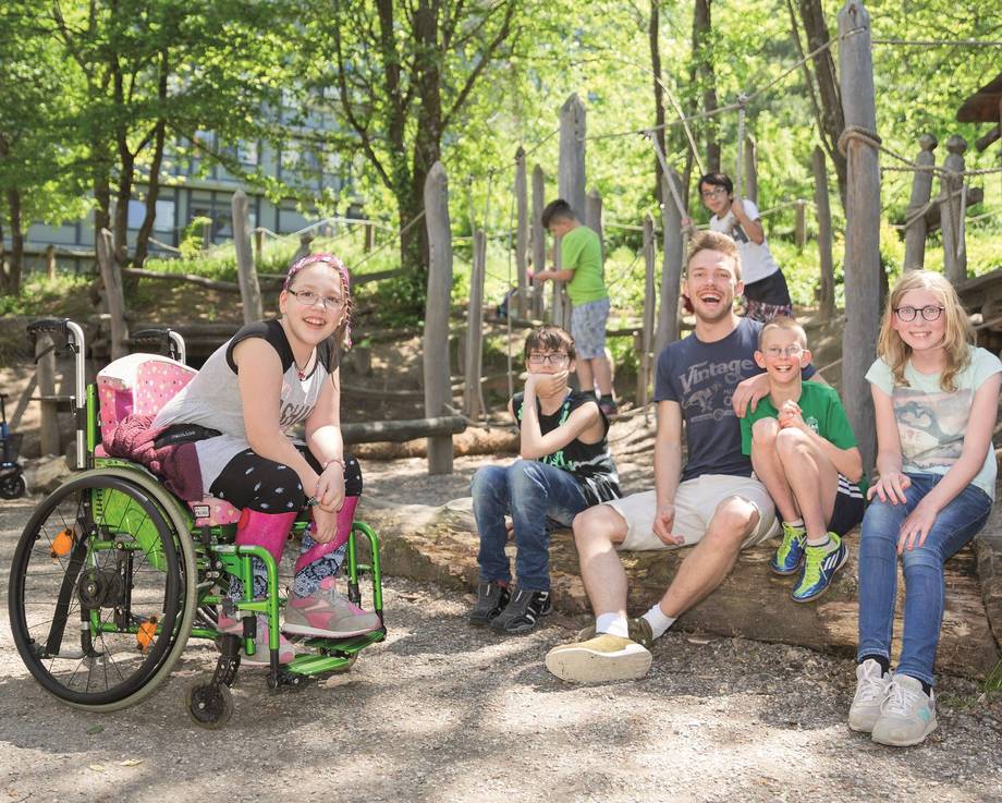 Schüler:innen und ein Erzieher sitzen nebeneinander auf einem liegenden Baumstamm.
